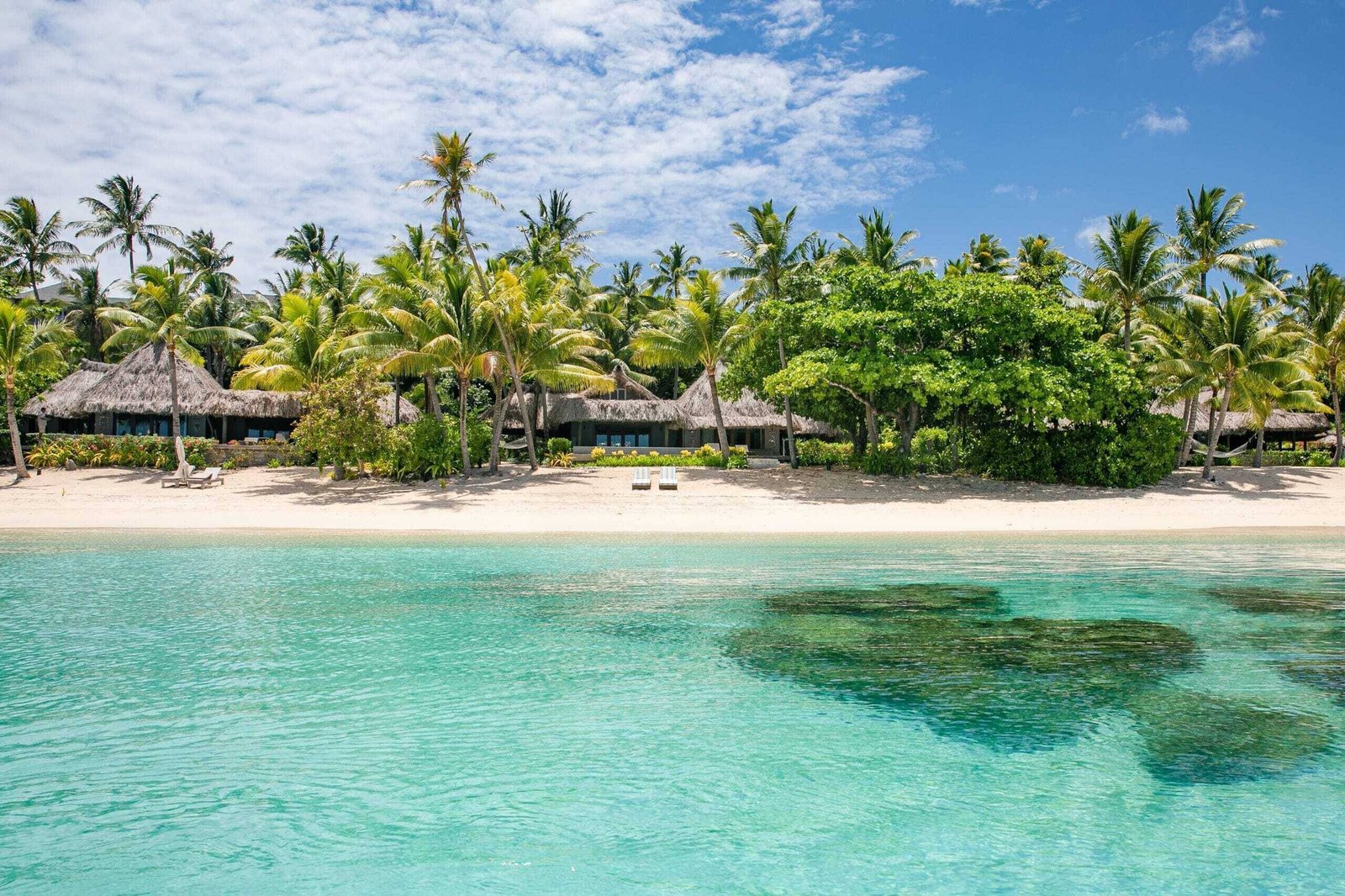 Thatched beachfront villas behind a palm line, fronting the lagoon at Kokomo Private Island