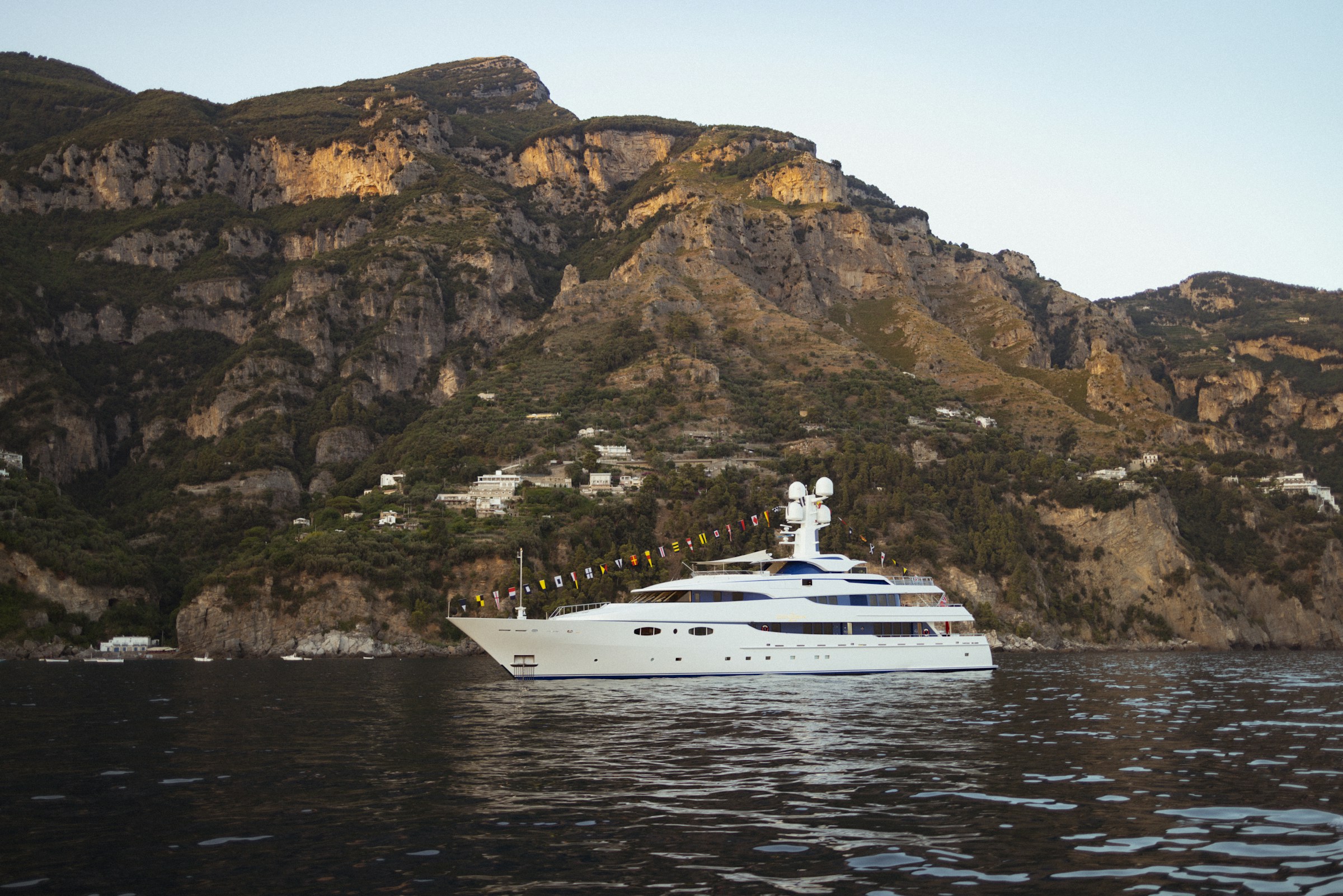 A white superyacht anchored beneath the Amalfi cliffs at golden hour
